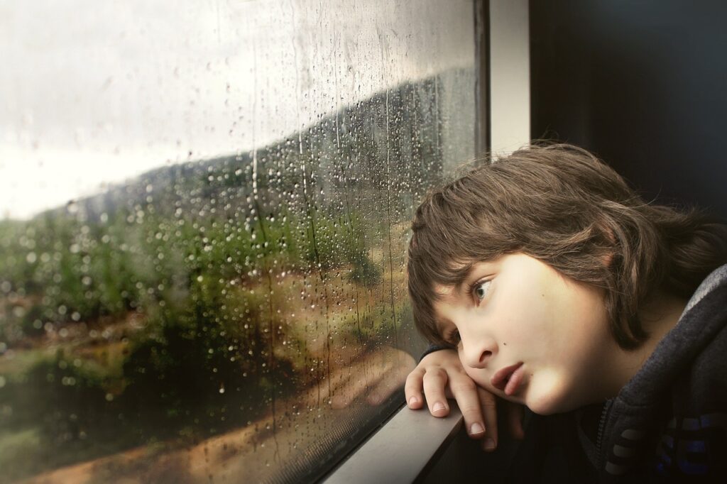 disappointed boy looking out a rainy window 