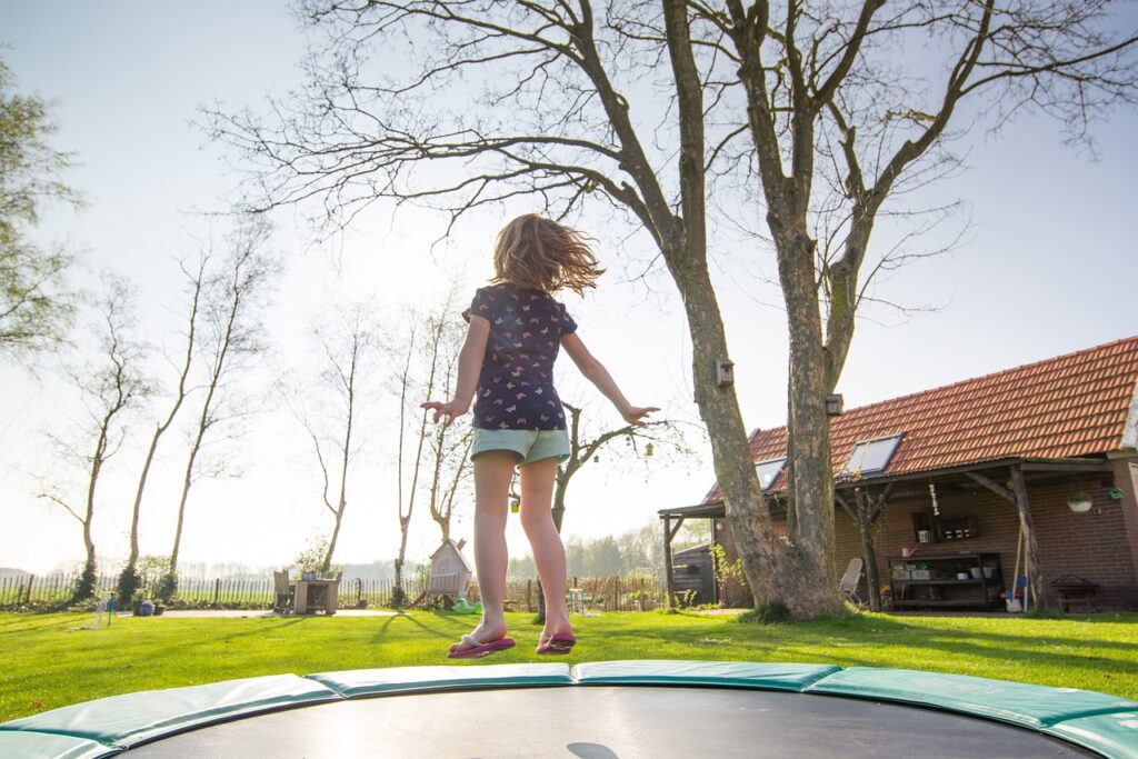young girl jumping on a trampoline with arms extended on a sunny day 